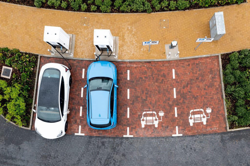 An aerial view directly above electric cars being charged at a motorway service station car charging station.
