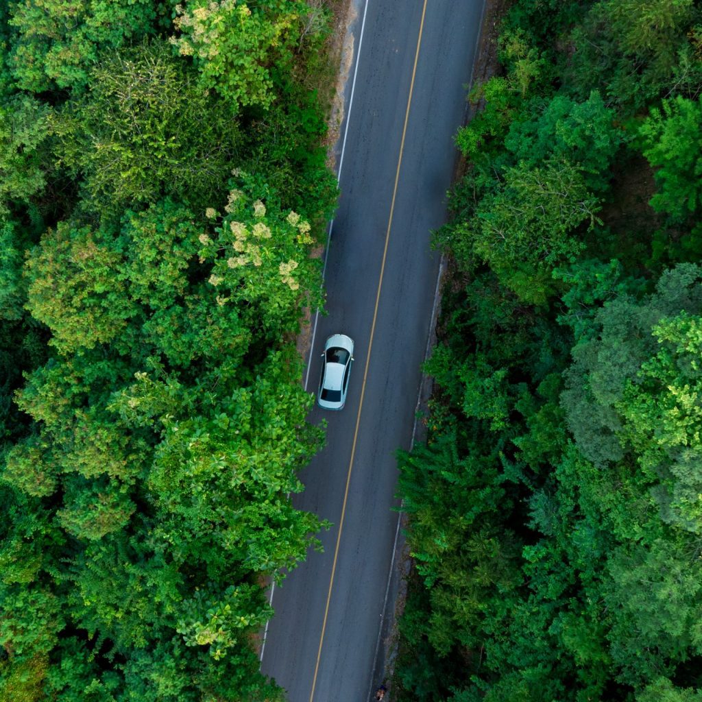 Aerial view of dark green forest road and white electric car Natural landscape and elevated roads Adventure travel and transportation and environmental protection concept.